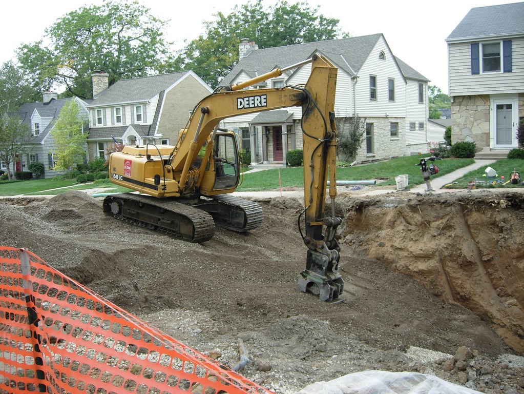 Excavator digging a sewer line trench on a residential street